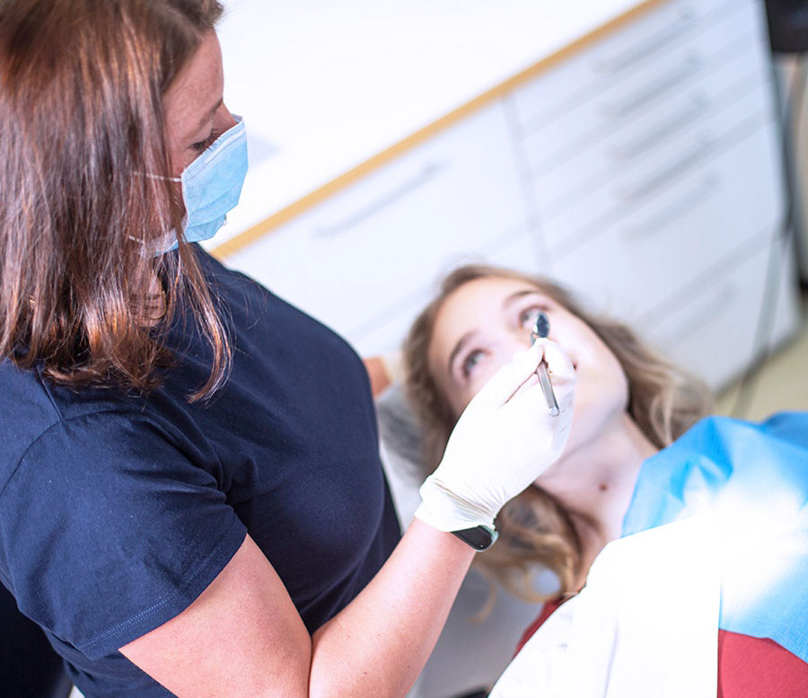 Zahn-Behandlung durch eine zahnmedizinische Fachkraft bei einer Patientin im Behandlungsstuhl
