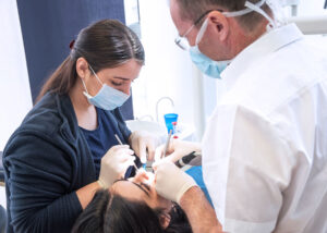 Zahnarzt und Assistenz behandeln eine Patientin im Behandlungsstuhl.