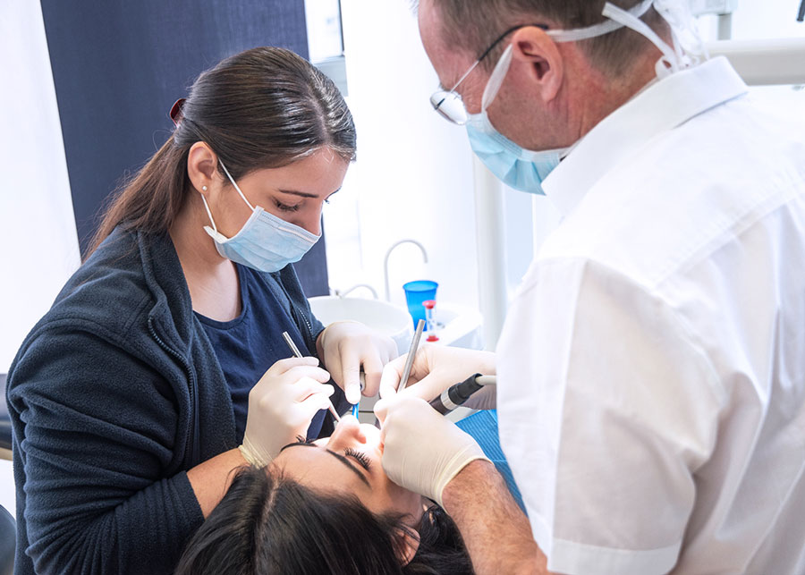Zahnarzt und Assistenz behandeln eine Patientin im Behandlungsstuhl.