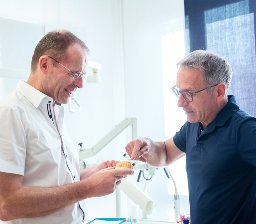 Zahnarzt erklärt einem Patienten den Ablauf am Zahnmodell.